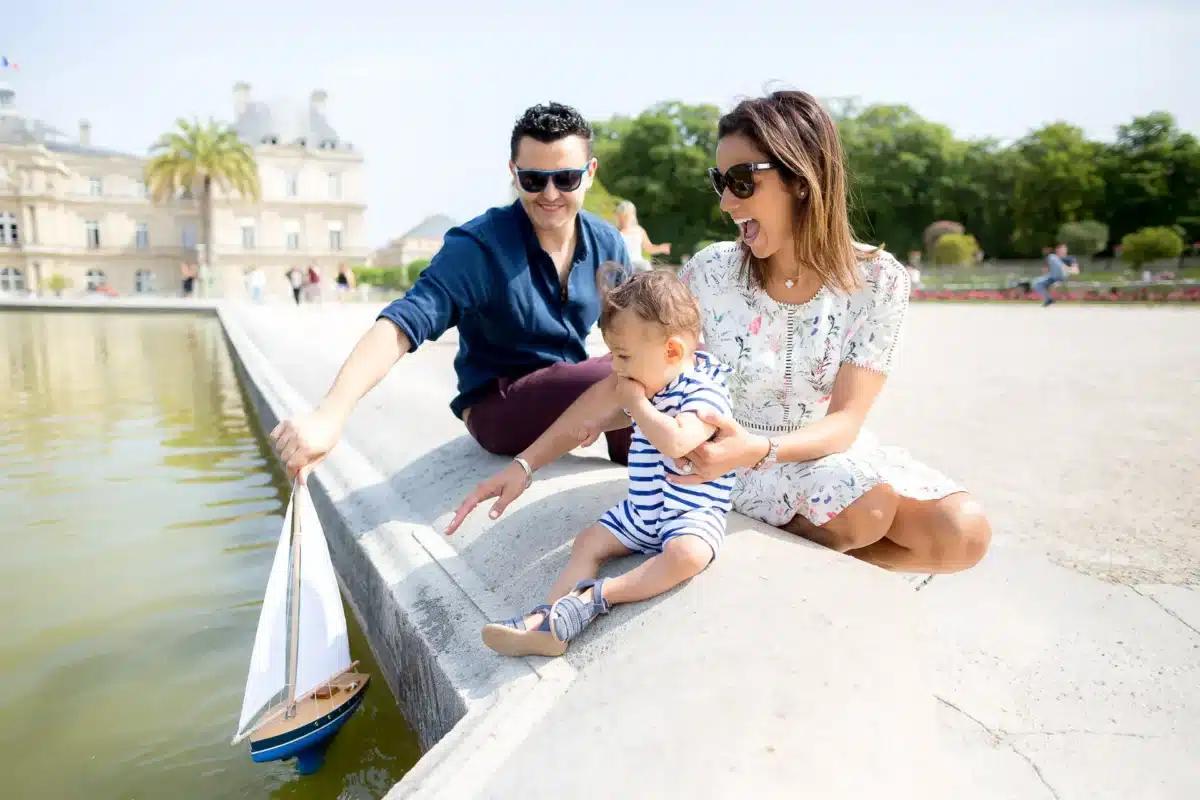 faq photographe puteaux - photo de famille jouant avec un bateau sur l'eau dans un parc à paris